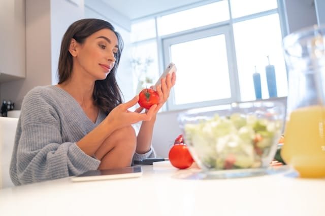 Femme d'une quarantaine d'années assise à sa table, devant une assiette légère, le regard songeur, comme beaucoup de celles qui pensent manger trop peu